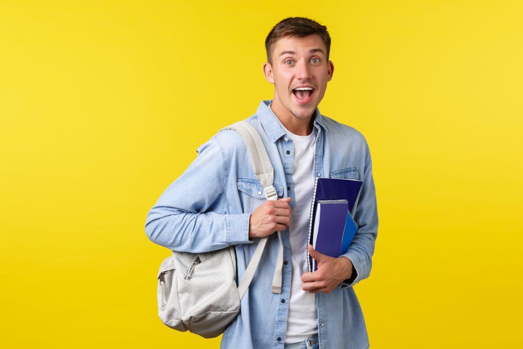 Egzamin z Angielskiego - education courses university concept surprised happy smiling guy seeing something amazed while heading class college board school holding backpack with notebooks