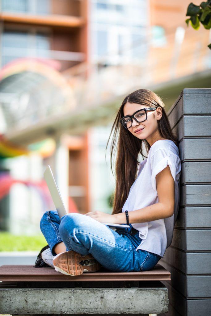 Matura Podstawowa - side view young woman eyeglasses sitting bench park using laptop computer
