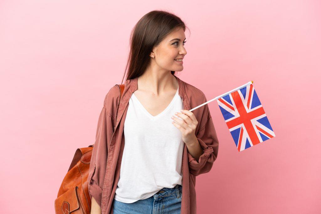 Matura Rozszerzona Angielski - young caucasian woman holding united kingdom flag isolated pink background looking side
